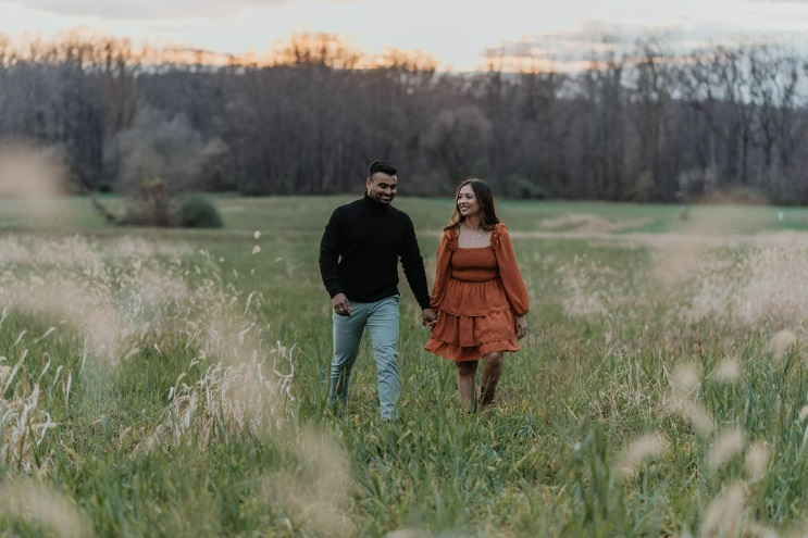 Couple holding hands in a grassy meadow at their fall engagement photo shoot.